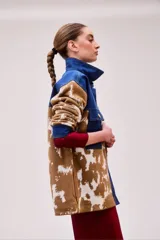 Chaqueta con corte camisero, cuello y solapa de jeans color índigo. Tejido que llega bajo la cadera con bolsillos laterales. Pattern de vaca en tonos café y crudo en las mangas y parte inferior.