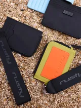 Billetera tarjetero negra de poliuretano con cierre y correa para colgar al cuello con logo Rusty estampado.