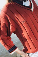 Buzo tejido verde con escote en V, cuello con rayas blancas y azul marino, y puños y ruedo con detalle de rayas.