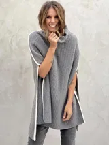 Poncho tejido de punto grueso color gris con cuello alto y aberturas laterales con ribete blanco.