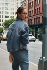 Cazadora de denim celeste de corte recto, con cuello solapa, manga larga, bolsillos delanteros de plastrón y cierre frontal con botones metálicos.