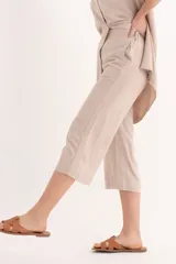 Conjunto de dos piezas color beige claro, compuesto por una camisa de manga corta con cuello y botones frontales, y un pantalón palazzo de tiro alto con detalle envolvente asimétrico en la parte delantera.