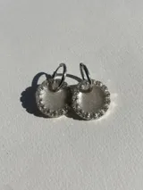 Aros colgantes con forma circular, hechos de resina color lila y borde de strass plateado. El aro es de acero quirúrgico plateado.