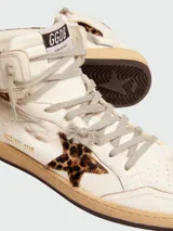 Championes de caña alta Golden Goose modelo Sky-Star, confeccionados en cuero color blanco con efecto desgastado. Presentan detalles en piel de poni con estampado de leopardo en la estrella lateral y el cuello. Incluyen cordones grises y etiqueta GGDB en la lengüeta.