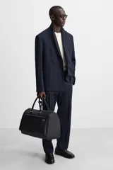 Bolso de viaje negro con textura grabada, compartimento principal con cierre de cremallera, bolsillo interior con cremallera, bolsillo frontal con cremallera, asa de hombro removible y ajustable.
