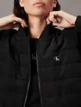 Campera bomber acolchada negra Calvin Klein, con logo bordado en el pecho y el puño. Confeccionada con poliéster reciclado, cuello, puños y bajo de canalé, cierre de cremallera, bolsillos con botón de presión en la cintura y forro ligeramente acolchado.