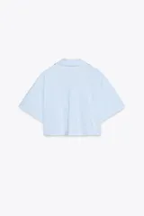 Camisa celeste de popelín con cuello solapa, escote pico y manga corta. Presenta dos bolsillos delanteros de parche y cierre frontal con botones.