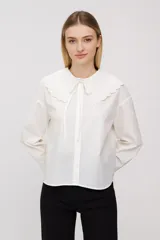 Blusa blanca de algodón con cuello babero bordado y lazos para atar.