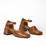 Zapato de cuero vacuno color marrón con pulsera al tobillo y hebilla. Tiene taco de madera forrado en cuero y suela de goma.