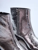 Bota corta plateada de cuero brillante con punta cuadrada y taco bajo negro.