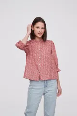 Blusa color ladrillo con estampado abstracto en tonos beige, cuello mao con volantes, mangas 3/4 abullonadas con puños elásticos y cierre frontal con botones.