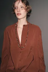 Camisa marrón de Zara Woman Collection confeccionada en hilatura con mezcla de lyocell. Tiene cuello redondo, manga larga acabada en puño, bajo asimétrico con aberturas laterales y cierre frontal con botones.