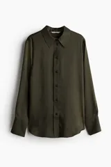 Camisa verde oscuro de manga larga con cuello clásico, cierre frontal con botones y puños abotonados. Confeccionada en tejido satinado con canesú y pliegue en la espalda. Bajo redondeado.