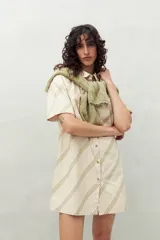 Vestido camisero corto color verde claro con estampado de hojas en blanco. Tiene cuello camisero, cierre frontal con botones y corte recto.