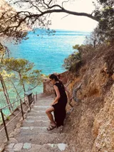 Vestido largo tejido de algodón color negro, sin mangas, con cuello redondo y tajos laterales. Presenta dos bolsillos de cuero color marrón en el frente.