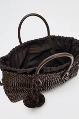 Bolso de mano marrón con cuerpo trenzado y doble asa. Incluye charm extraíble y bolsa interior con cierre fruncido.
