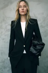 Blazer negro largo con cuello solapa, manga larga con hombreras, bolsillos delanteros de vivo y cierre frontal con un botón.