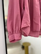 Camisa rosa de manga larga con puños, cuello mao y cierre frontal con botones. Tiene corte y frunce en la parte delantera.