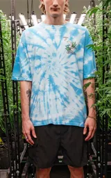Remera celeste con efecto tie-dye, corte extra oversize, hombros caídos y cuello redondo. Estampa pequeña en el pecho con un personaje fumando sobre una hoja de marihuana.