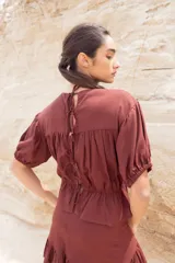 Blusa color chocolate con cuello redondo, mangas cortas abullonadas, detalle de flores bordadas en el frente y corte con volantes en la cintura.
