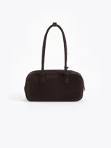 Cartera rectangular de estructura firme confeccionada en cuero descarne vacuno color marrón. Presenta manijas fijas, cierre superior y un charm metálico dorado en forma de vaquita de San Antonio colgando de un tag lateral. Incluye el logo de la marca grabado en relieve en el frente.