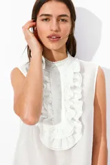 Blusa blanca sin mangas con cuello mao y pechera de volados con bordados de encaje.