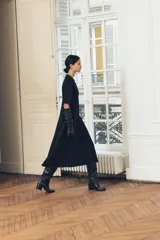 Vestido midi negro de cuello redondo y manga corta, con bolsillos laterales ocultos y costuras marcadas. Tiene corte evasé con abertura en la espalda y cierre trasero con cremallera oculta.