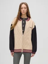 Saco estilo bomber color beige, con mangas negras y detalles en bordó. Presenta cierre frontal, cuello y puños acanalados a rayas, y un logo bordado en el pecho.