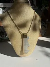 Collar con cordón fino color ocre, dije de nácar blanco con forma irregular y aplique metálico dorado.