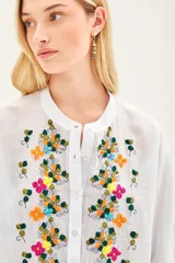 Camisa blanca de voile con rayas finas, corte amplio, cartera con botones y bordado de flores en el frente.