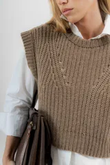 Chaleco de lana color crema, tejido a punto perlado con calado en la parte delantera. Tiene cuello a la base y silueta cuadrada.