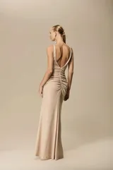 Vestido largo color champagne con escote en V, breteles finos, detalle de nudo en la cintura y abertura lateral en la falda.