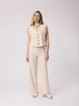 Pantalón de vestir color beige, de corte recto, con bolsillos laterales y traseros. Se ajusta a la cintura con cinturón de cuero marrón.