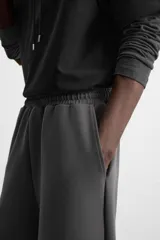 Pantalón jogger wide fit color gris oscuro, confeccionado en tejido de algodón compacto con elasticidad. Cuenta con cintura elástica ajustable con cordón, pliegues frontales, bolsillos delanteros y bolsillo trasero de parche.