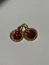 Par de aros colgantes con dije circular de resina color marrón con glitter, bordeado con strass y arito de acero quirúrgico dorado.