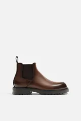 Bota Chelsea de cuero color marrón con elástico lateral y tirador trasero. Suela track de goma negra.