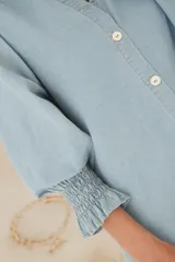 Vestido camisero corto de denim celeste, con cuello mao, mangas 3/4 con elástico en los puños y cierre frontal con botones de nácar.