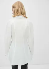 Camisa blanca de corte recto con cuello camisero, mangas largas con puños abotonados y cierre frontal oculto con botones.