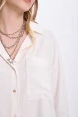 Camisa blanca de lino de manga larga con cuello clásico, cierre frontal con botones y bolsillo en el pecho.