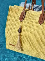 Bolso de playa amarillo tejido con asas de cuero marrón y detalle de borla con cuentas. Interior forrado con tela celeste.