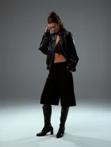 Chaqueta bomber negra de cuero sintético con cierre frontal y cuello clásico.