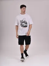 Remera blanca de corte recto con estampado de un auto clásico frente a un skyline urbano.