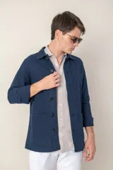 Sobre camisa color beige confeccionada en lino, de corte recto, con cuello clásico, manga larga con puños abotonados, cierre frontal con botones a tono, bolsillo de parche en el pecho y ruedo recto.