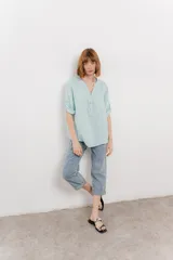 Camisa celeste de lino con cuello mao, escote en V abotonado, bolsillo frontal y mangas 3/4 arremangables.