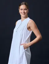 Vestido corto blanco de algodón y rayón, sin mangas, con cuello a la base, abertura central con botones y detalle plisado en la delantera. Incluye bolsillos laterales.