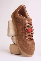 Zapatillas bajas marrones de gamuza con cordones y detalle de aplique de fresa en los cordones.