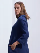 Vestido camisero blanco de algodón con cuello solapa, escote en V y mangas 3/4 regulables. Presenta bolsillos laterales verticales y abertura con botones en la espalda.