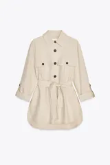 Camisa color beige de cuello solapa y manga larga acabada en vuelta con trabilla y botón. Bolsillos delanteros de plastrón con solapa. Bajo con aberturas laterales. Cierre frontal con botones y cinturón del mismo tejido.