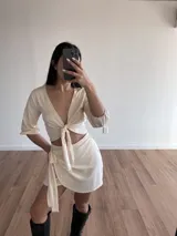 Conjunto color crudo compuesto por un top corto con escote en V y mangas 3/4 abullonadas, con cierre frontal anudado, y una minifalda cruzada con lazo lateral.