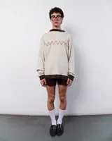 Sweater tejido color crema con cuello y puños marrones. Presenta un bordado manual en forma de zig-zag color rojo.